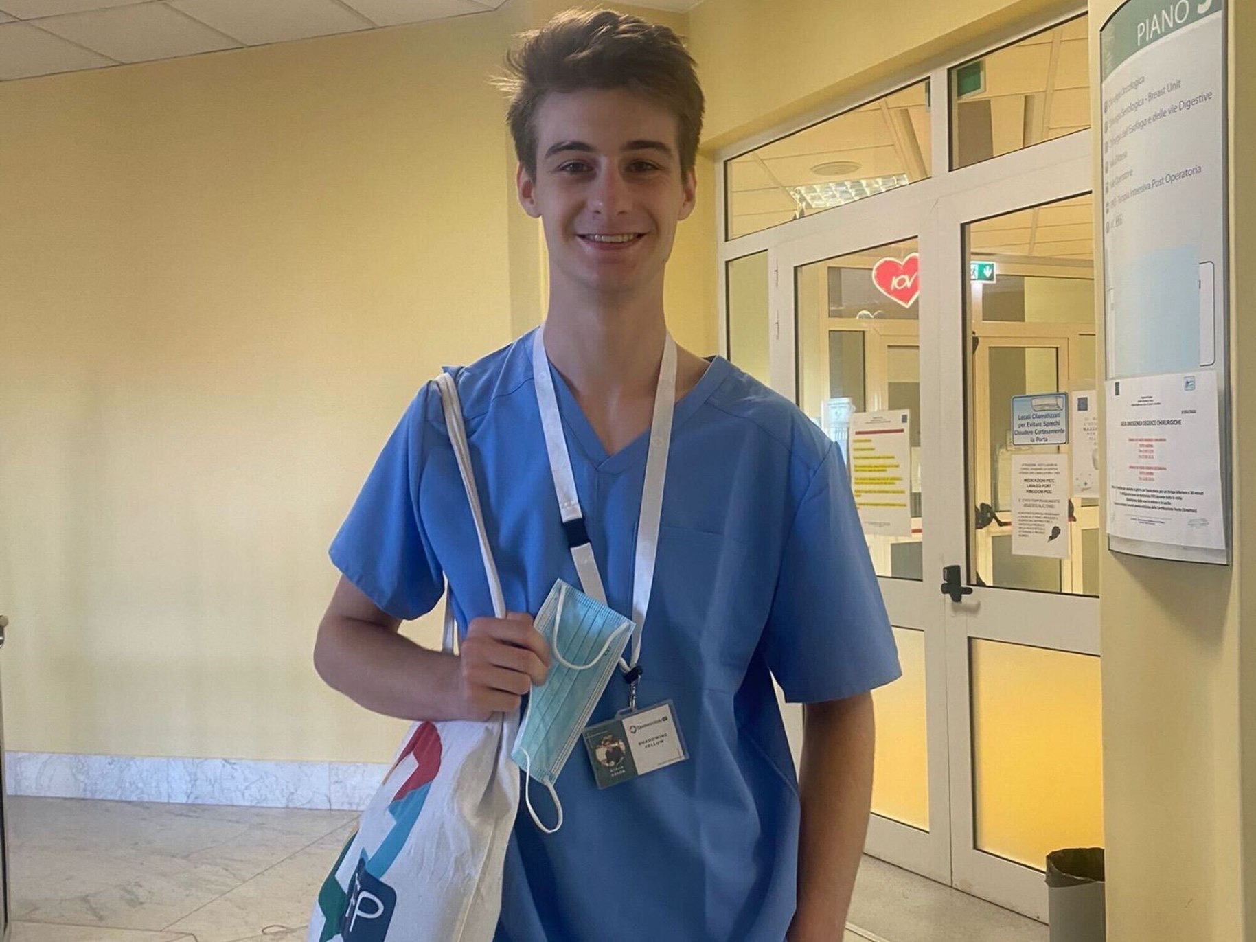 Aidan stands in front of the hospital in his scrubs.