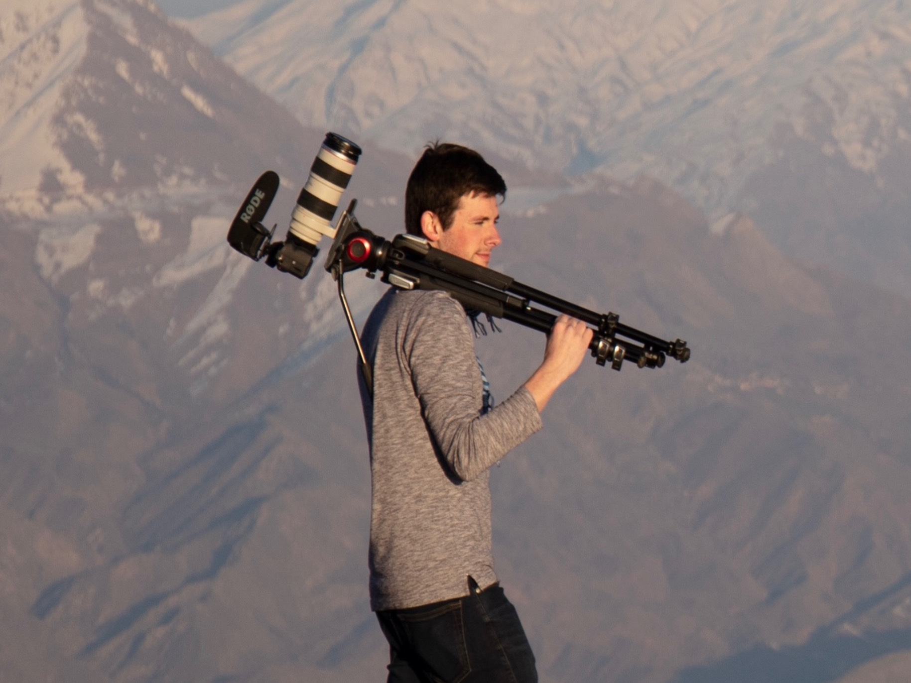 tom stands with a camera over his shoulder as he overlooks a mountain range